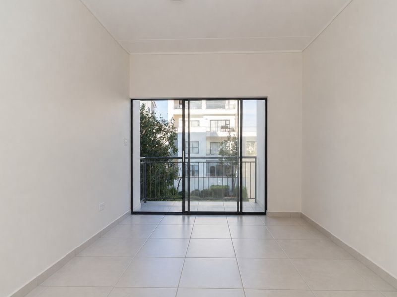 A bright, empty living area featuring neutral tiled flooring and large sliding glass doors that open onto a private balcony.