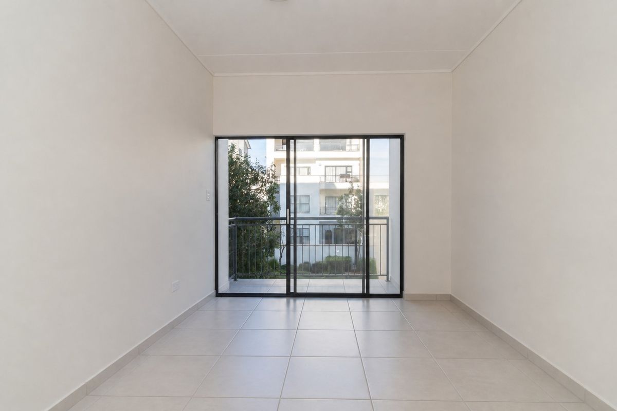 A bright, empty living area featuring neutral tiled flooring and large sliding glass doors that open onto a private balcony.
