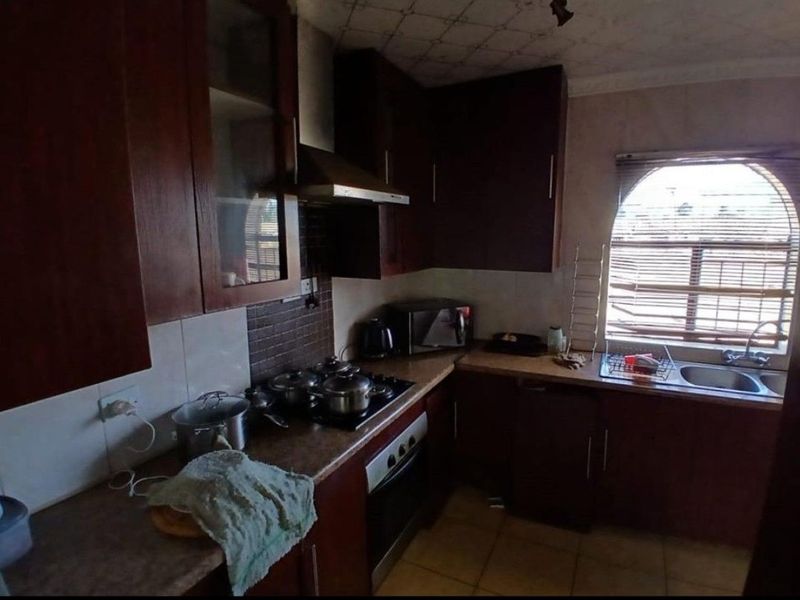 A compact kitchen featuring dark wood cabinetry, laminate countertops, a built-in oven with gas hob, and a double bowl sink under an arched window.
