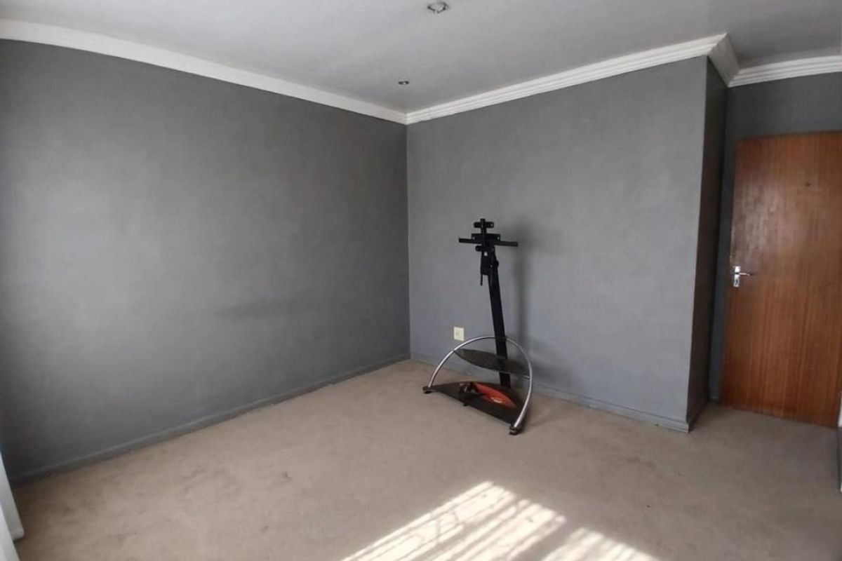 A spacious, empty bedroom featuring neutral grey walls, recessed ceiling downlights, decorative coving, and carpeted flooring.
