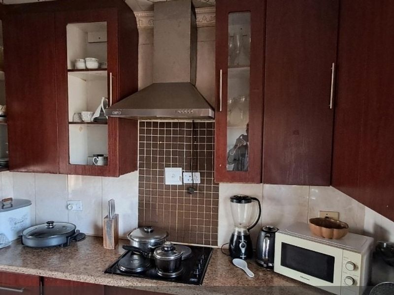 A functional kitchen featuring dark wood cabinetry, a stainless steel extractor fan, and a mosaic tile splashback with a granite-look countertop.