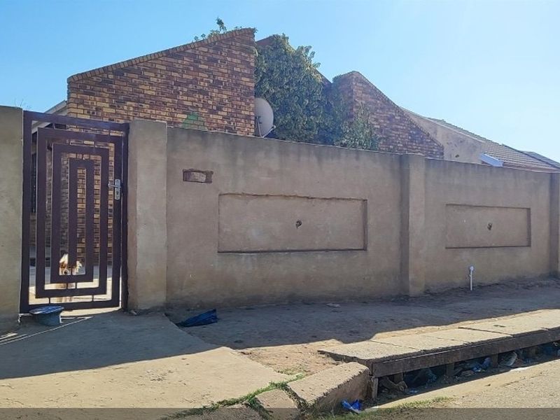 Front exterior view of the property featuring a brick facade, a solid boundary wall, and metal pedestrian and driveway gates.