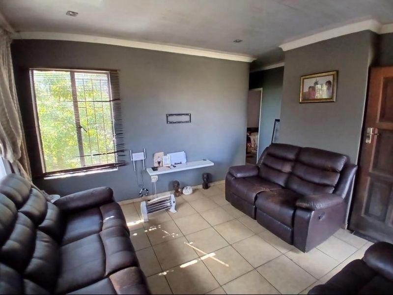 A living room featuring tiled flooring, ceiling cornices, and security bars on the window, providing a functional space with potential for cosmetic updates.