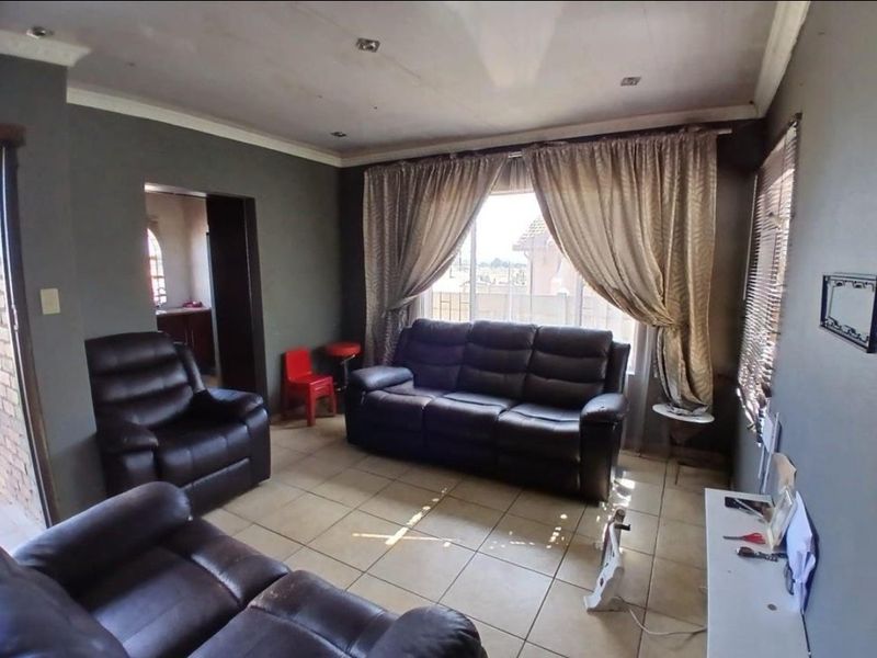 A living room featuring tiled flooring, recessed downlighting, and decorative cornicing, with visible signs of ceiling wear.