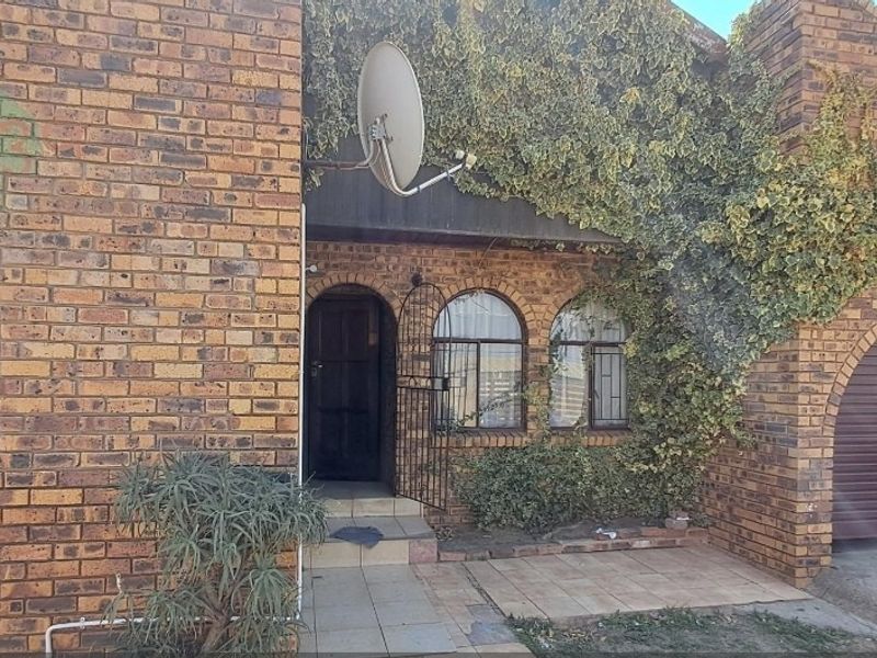 Front elevation of a face brick house featuring arched windows, an arched garage door, and a tiled entrance porch with security gate.