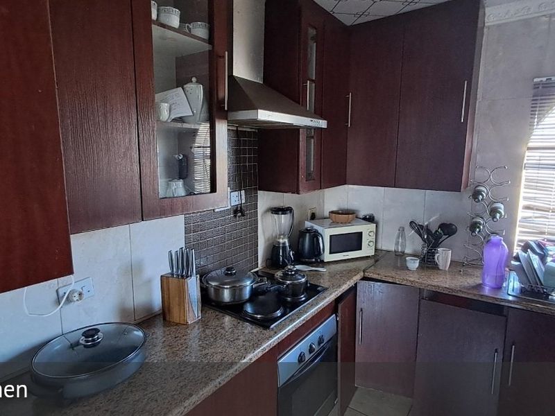 A functional kitchen featuring dark wood cabinetry, granite countertops, a built-in oven, and an electric hob with a stainless steel extractor fan.