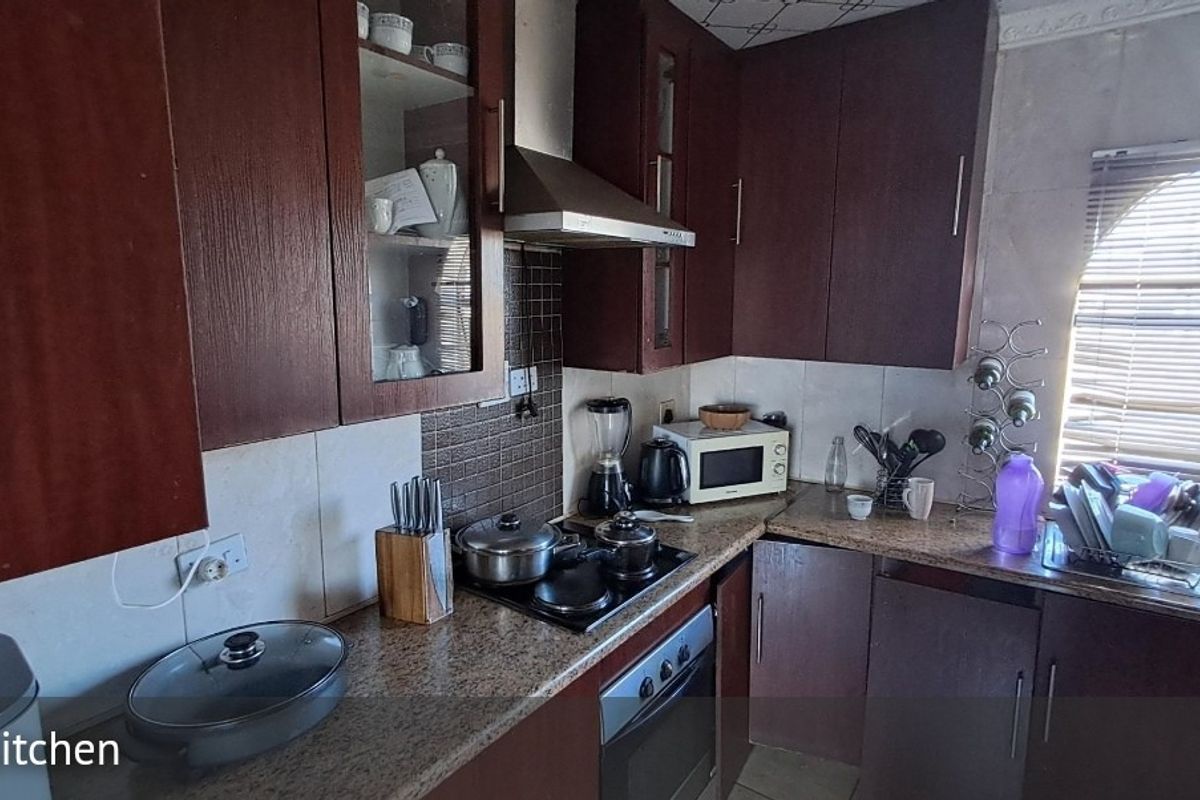 A functional kitchen featuring dark wood cabinetry, granite countertops, a built-in oven, and an electric hob with a stainless steel extractor fan.