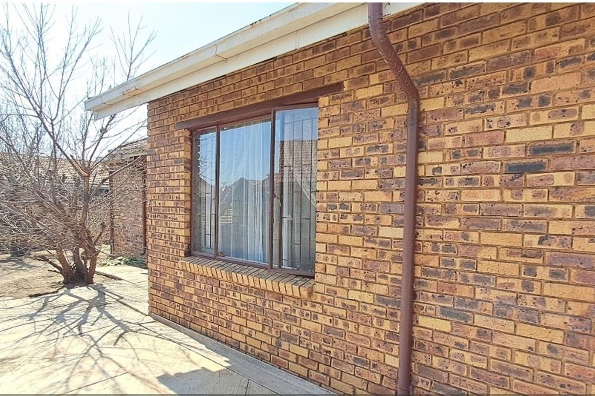 Rear exterior view of the house featuring face brick walls, a paved patio area, and secure window and door fittings.