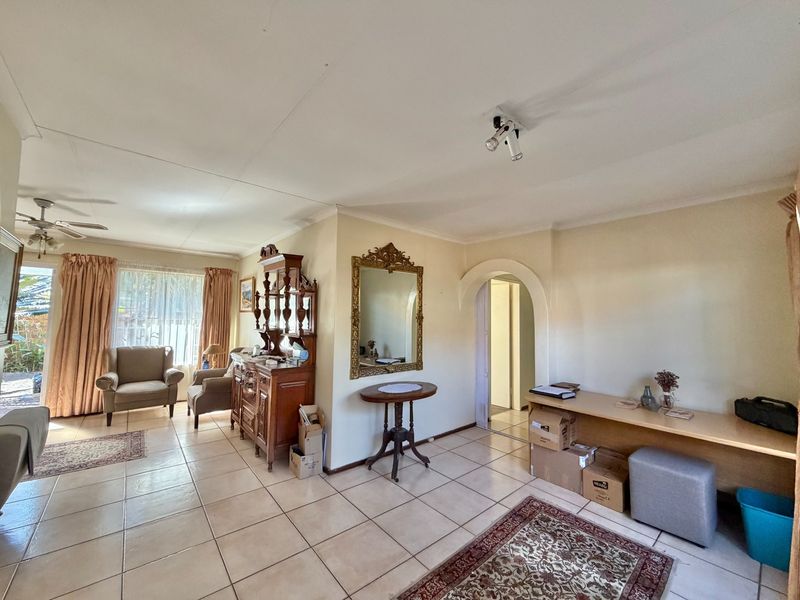 A spacious living area featuring ceramic floor tiles, a decorative archway, and a built-in desk, offering a functional layout with natural light.