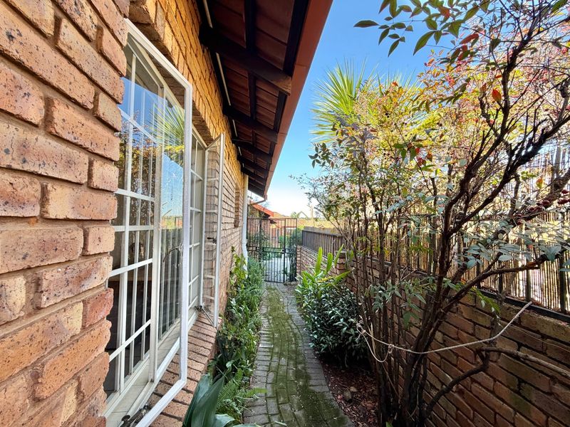 A side pathway featuring brick walling, paved flooring, and a metal security gate leading to the rear garden area.