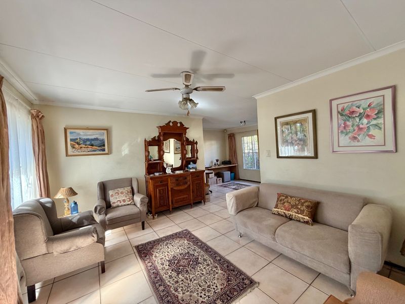 Spacious living room featuring neutral ceramic floor tiles, a ceiling fan, and natural light through large windows with security bars.