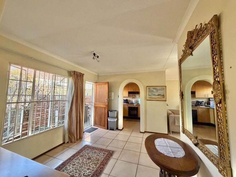 A living area featuring tiled flooring, an arched entryway leading to the kitchen, and large windows with security bars.