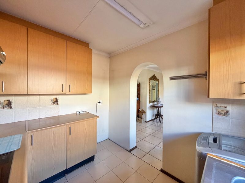 A functional scullery area featuring laminate cabinetry, tiled splashbacks, and an arched doorway leading to the adjacent living space.