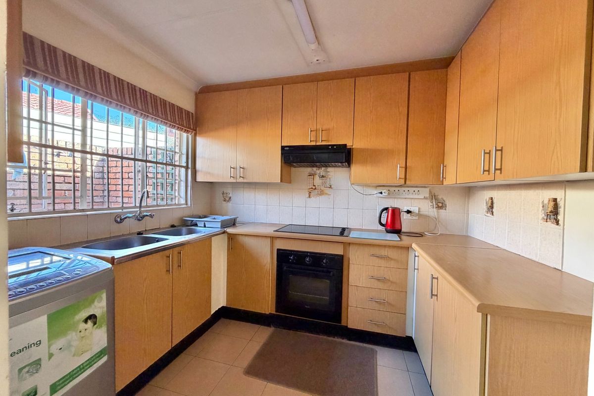 Functional kitchen featuring light wood-finish cabinetry, built-in oven, electric cooktop, extractor fan, and a double bowl stainless steel sink with tiled backsplash.