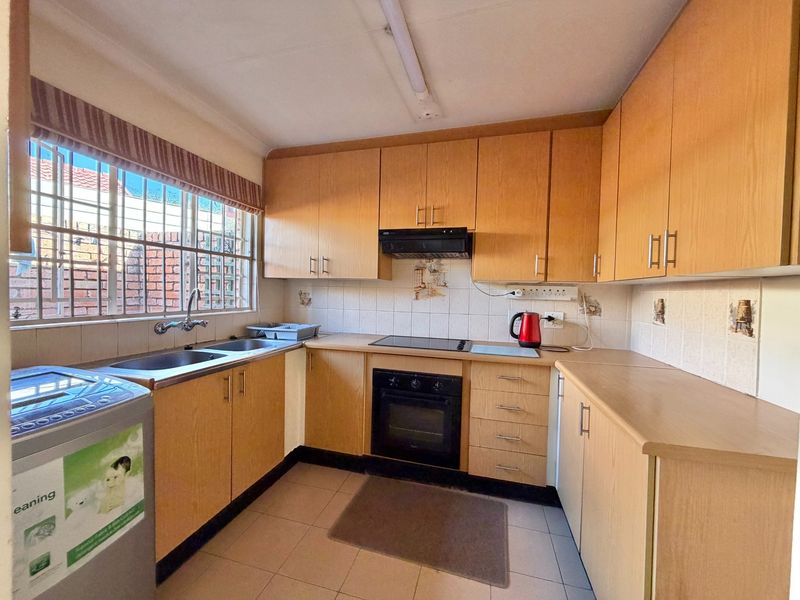 Functional kitchen featuring light wood-finish cabinetry, built-in oven, electric cooktop, extractor fan, and a double bowl stainless steel sink with tiled backsplash.