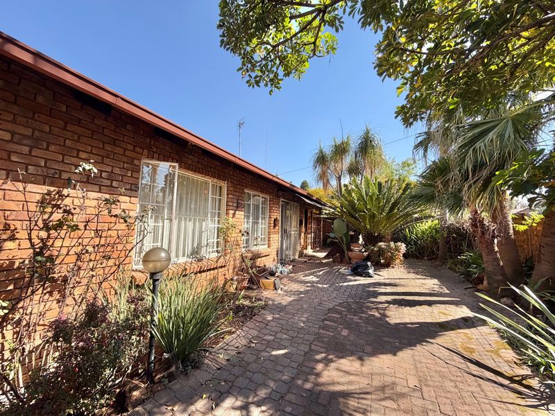 A rear exterior view of the townhouse featuring a brick facade, paved patio area, and established garden landscaping.