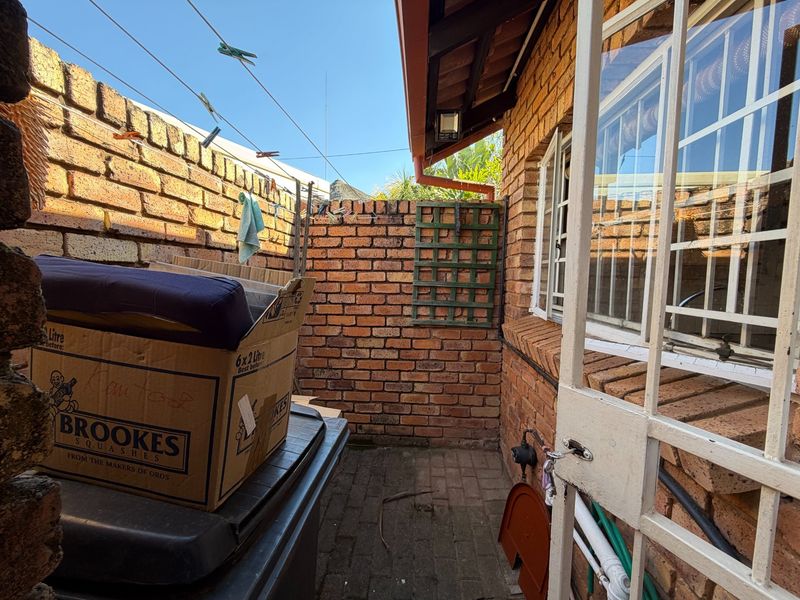 A narrow rear courtyard area featuring brick boundary walls, paved flooring, and security-fitted windows and doors.