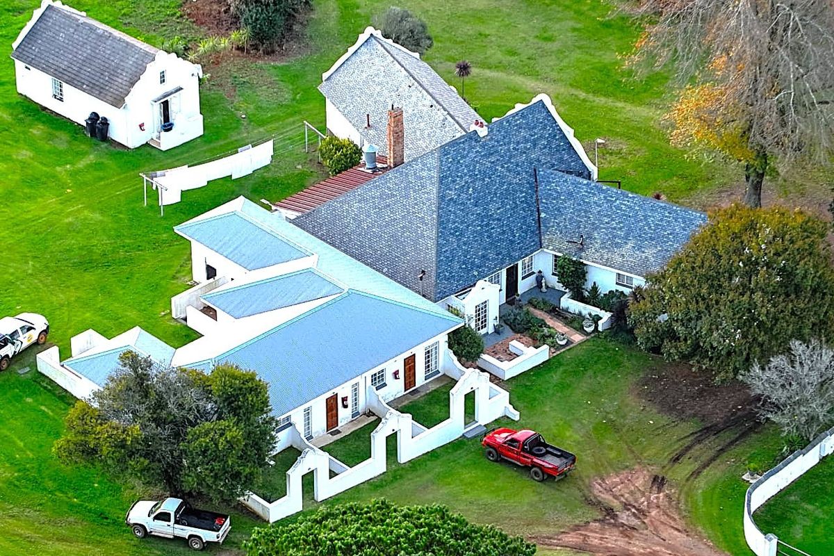 Aerial view of a farm property featuring a main residence with a pitched roof, a separate outbuilding, and surrounding landscaped grounds.