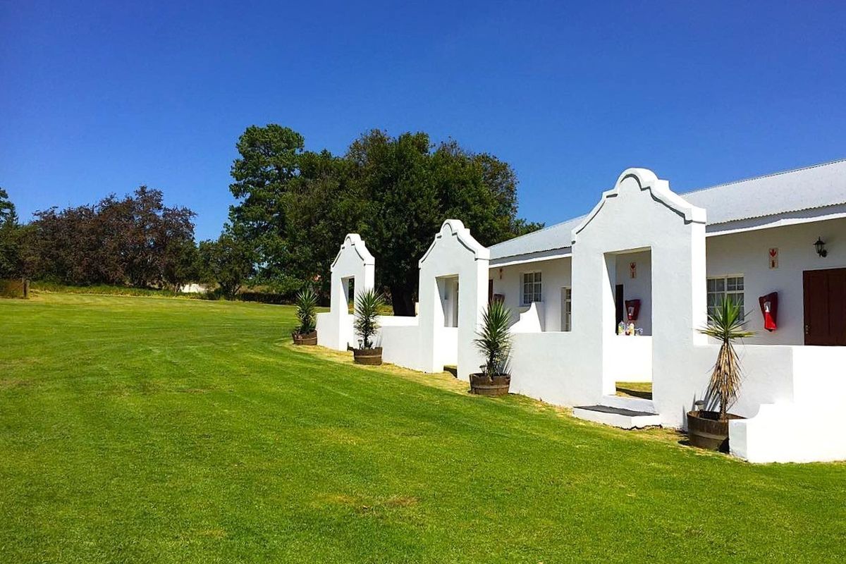A well-maintained farm building featuring white gabled parapet walls, a corrugated metal roof, and a spacious surrounding lawn area.