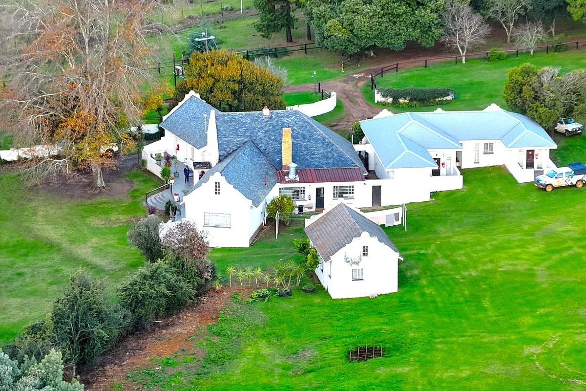 Aerial view of a farm property featuring a main residence with a pitched slate roof, an outbuilding, and expansive surrounding green lawns.