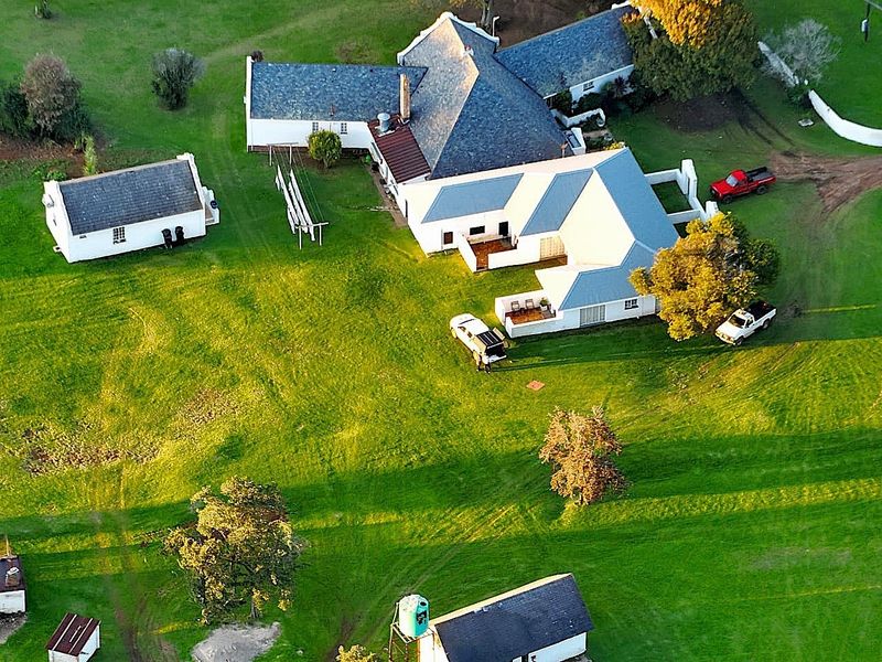 Aerial view of a farm property featuring a main residence with a pitched roof, a detached outbuilding, and surrounding green pasture land.