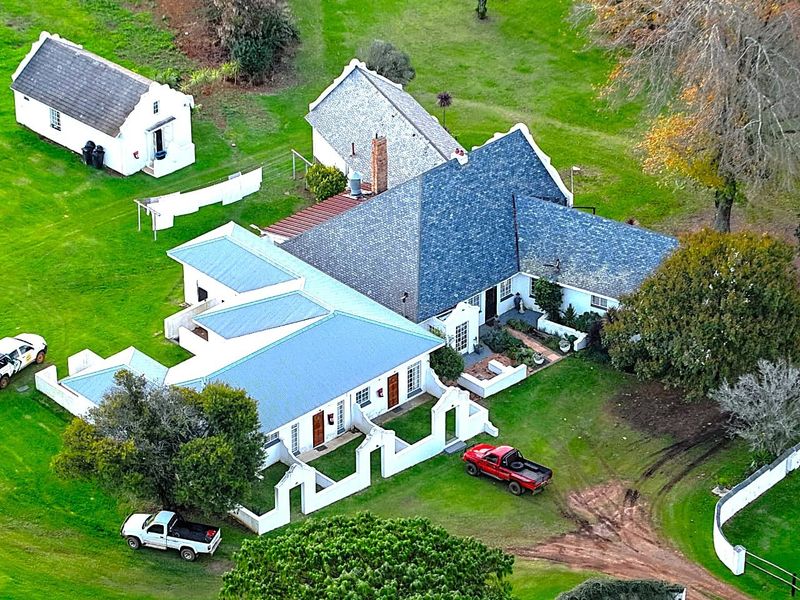 Aerial view of a farm property featuring a main residence with a pitched roof, a separate outbuilding, and surrounding landscaped grounds.