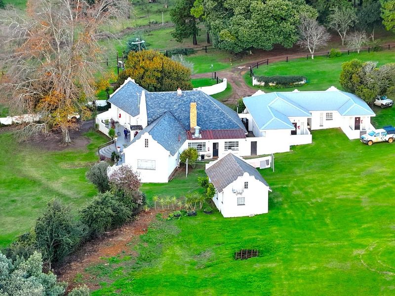 Aerial view of a farm property featuring a main residence with a pitched slate roof, an outbuilding, and expansive surrounding green lawns.