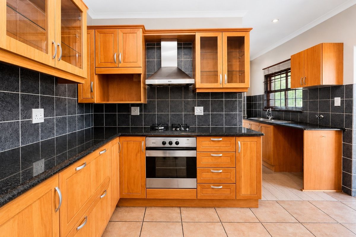 A well-maintained kitchen featuring wooden cabinetry, granite countertops, a built-in oven with gas hob, and a tiled backsplash.
