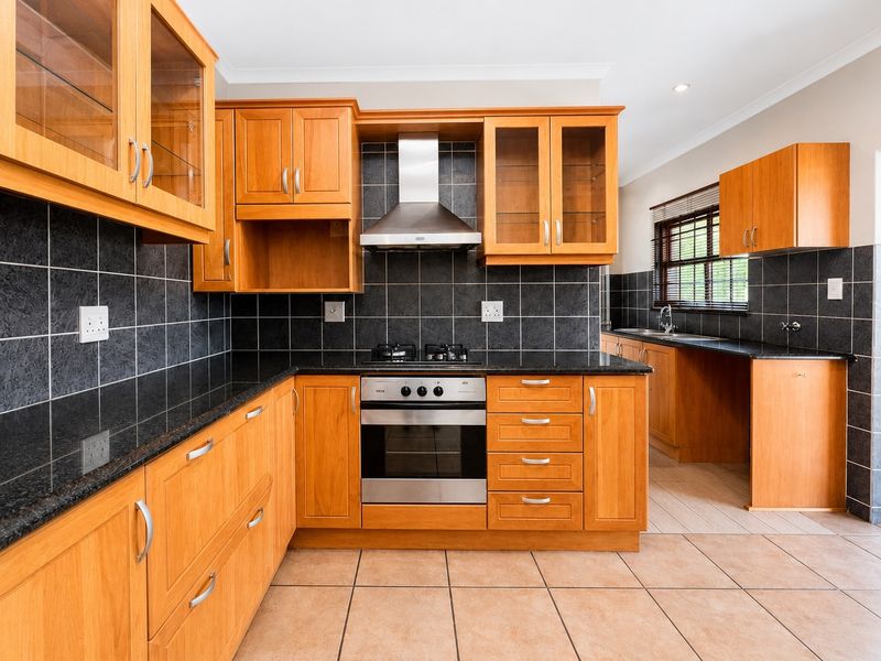 A well-maintained kitchen featuring wooden cabinetry, granite countertops, a built-in oven with gas hob, and a tiled backsplash.