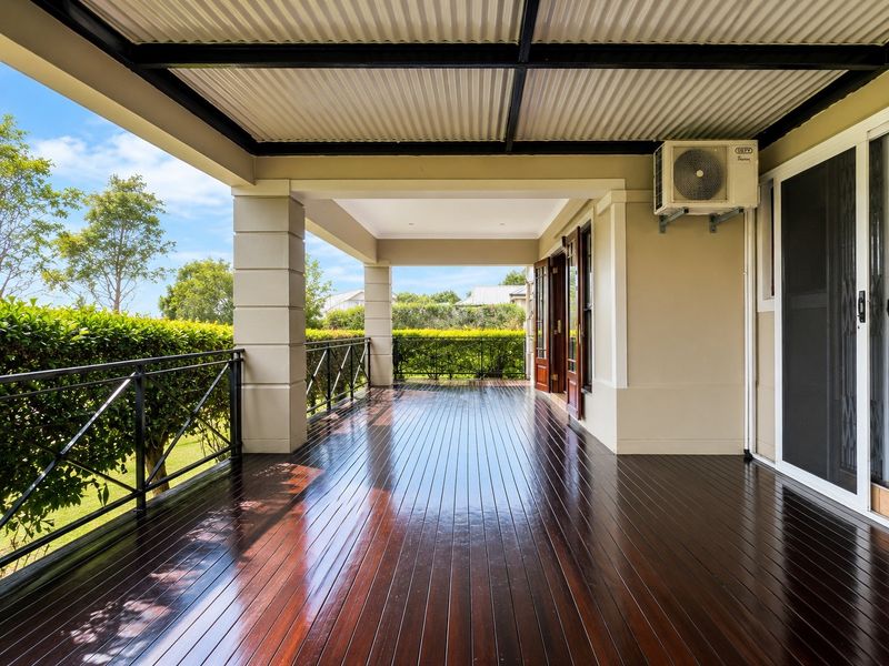 A spacious covered patio featuring polished timber decking, a corrugated metal roof, and a metal balustrade overlooking the garden.
