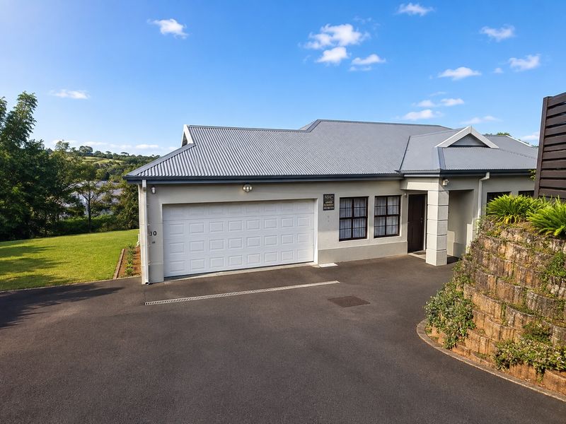 Front exterior view of the townhouse featuring a paved driveway, sectional garage door, and a well-maintained corrugated metal roof.