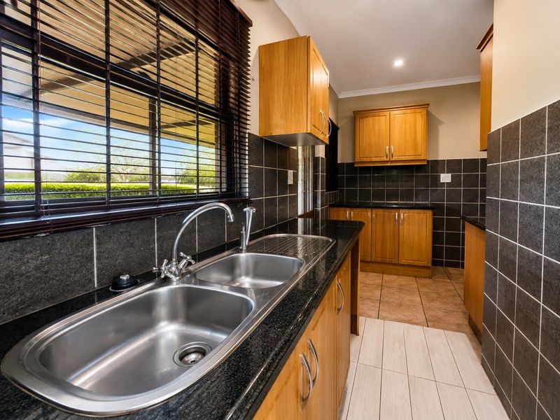 A clean, functional kitchen featuring wooden cabinetry, granite countertops, a double stainless steel sink, and dark tiled backsplash.