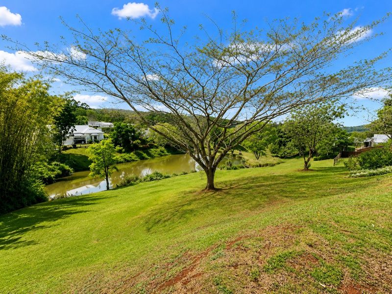 A scenic view of the estate grounds featuring a tranquil pond, manicured lawns, and mature trees under a clear blue sky.