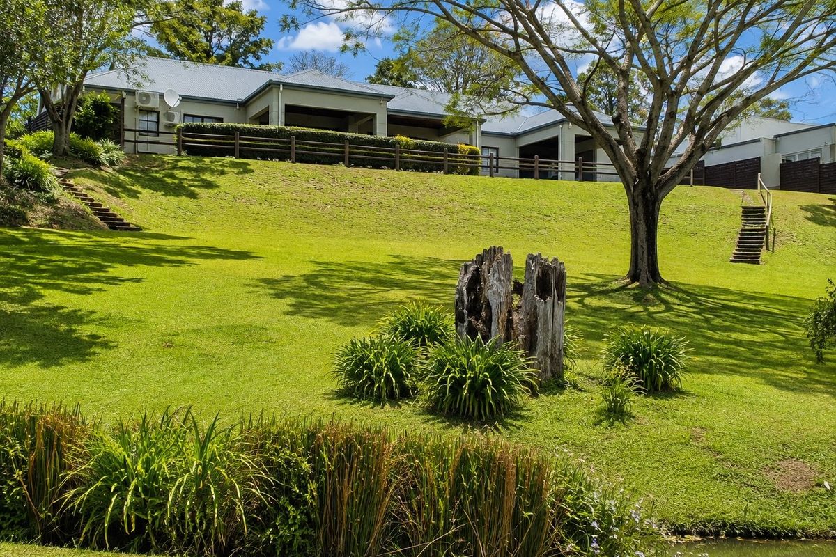 A view of the rear elevation of the townhouse, featuring a large landscaped lawn, timber fencing, and a covered patio area.