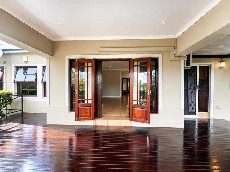 A spacious covered patio featuring polished timber decking, recessed lighting, and elegant timber french doors providing seamless access to the interior living space.