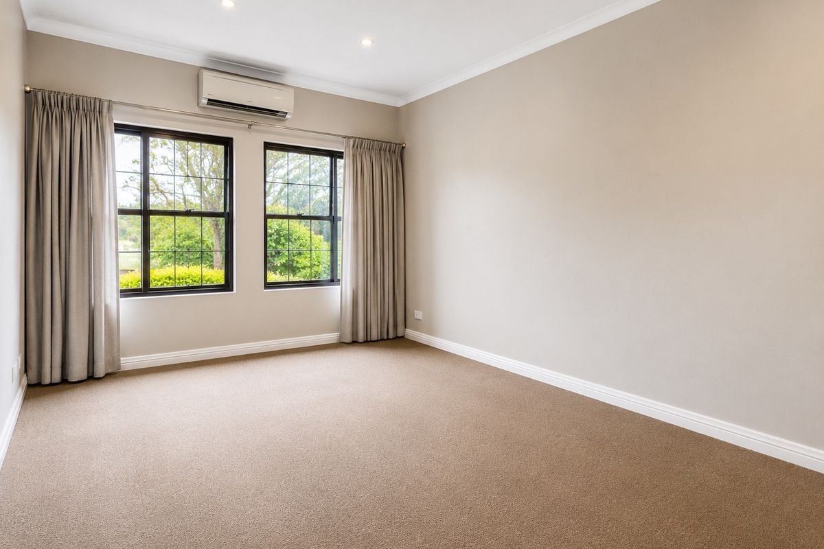 A bright, empty bedroom featuring neutral carpet, recessed downlighting, and a wall-mounted split-system air conditioner with views of the garden.