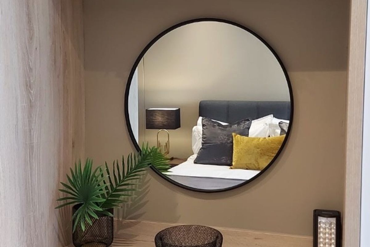 A well-appointed bedroom featuring a built-in wooden vanity unit with a floating shelf and a modern circular wall mirror.