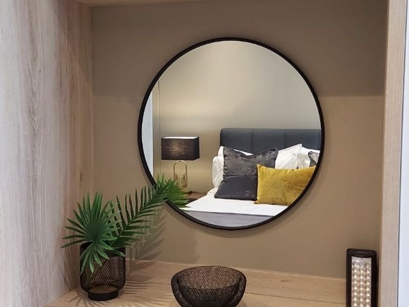 A well-appointed bedroom featuring a built-in wooden vanity unit with a floating shelf and a modern circular wall mirror.