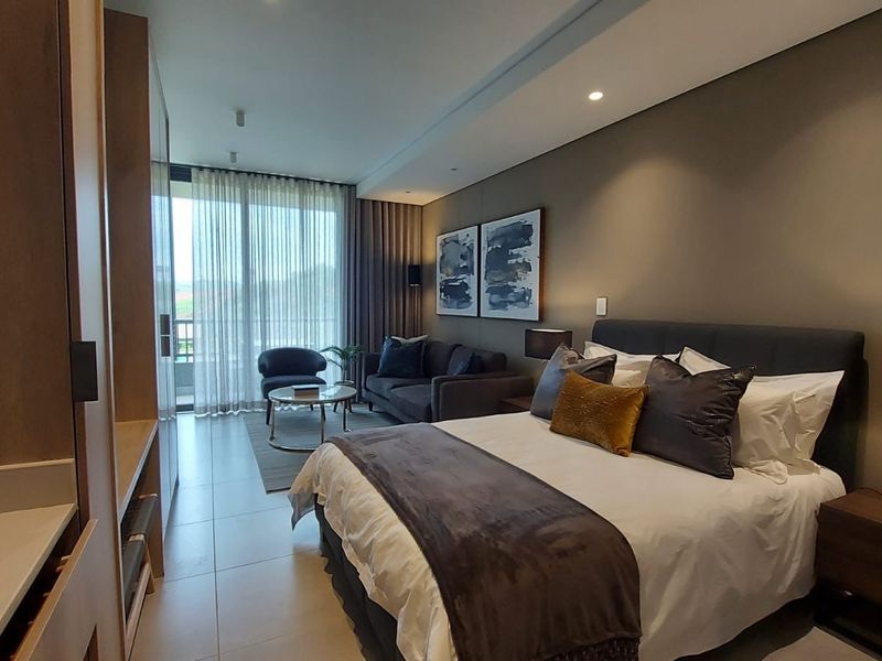 A modern, well-appointed bedroom featuring built-in cabinetry, recessed lighting, and direct access to a private balcony through large sliding glass doors.