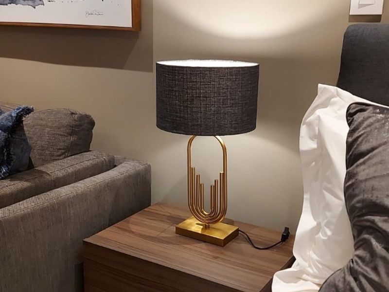 A close-up view of a bedroom corner featuring a modern bedside table, lamp, and neutral wall finishes.