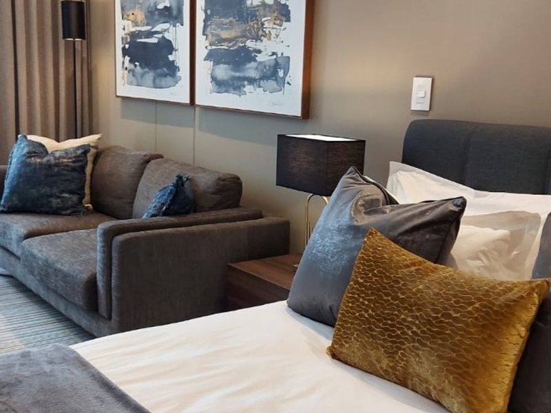 A well-appointed bedroom featuring neutral wall tones, recessed ceiling lighting, and integrated curtain tracks, creating a comfortable and modern living space.