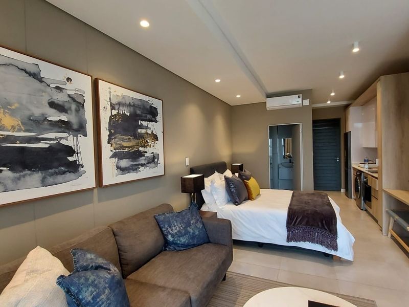 Modern open-plan studio apartment featuring a combined living and sleeping area with integrated kitchen cabinetry, tiled floors, and recessed lighting.
