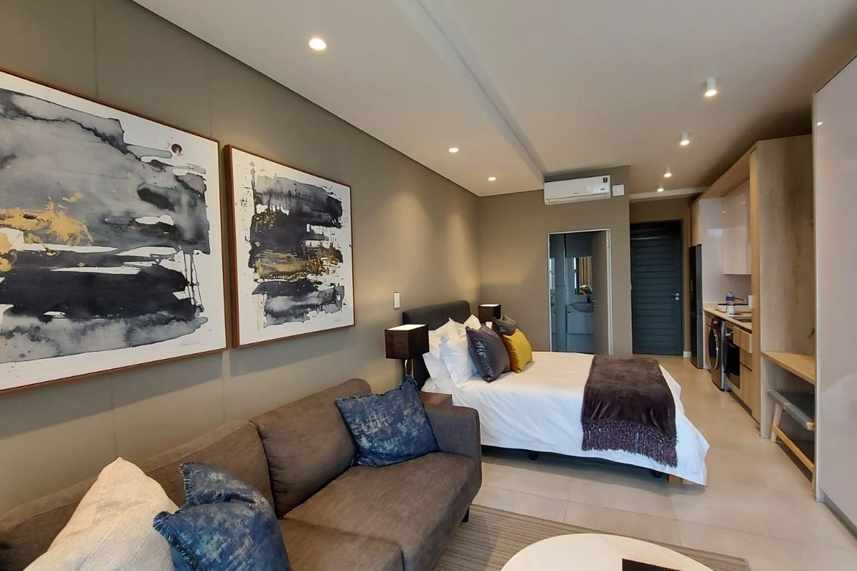 Modern open-plan studio apartment featuring a combined living and sleeping area with integrated kitchen cabinetry, tiled floors, and recessed lighting.