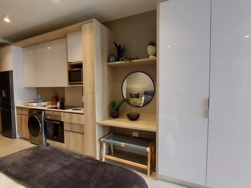 Modern open-plan studio apartment featuring a compact kitchenette with integrated appliances, built-in cabinetry, and a sleek wardrobe unit.