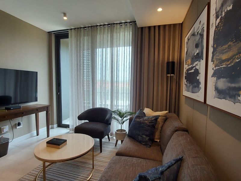 A modern, well-maintained living room featuring neutral tones, recessed lighting, and a large sliding glass door providing access to the balcony.