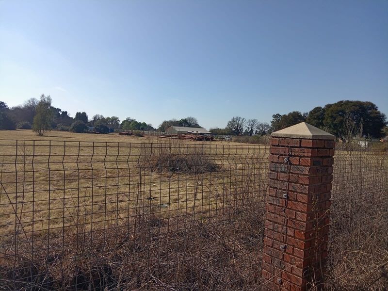 A view of an expansive open plot of land enclosed by wire mesh fencing and a brick pillar.
