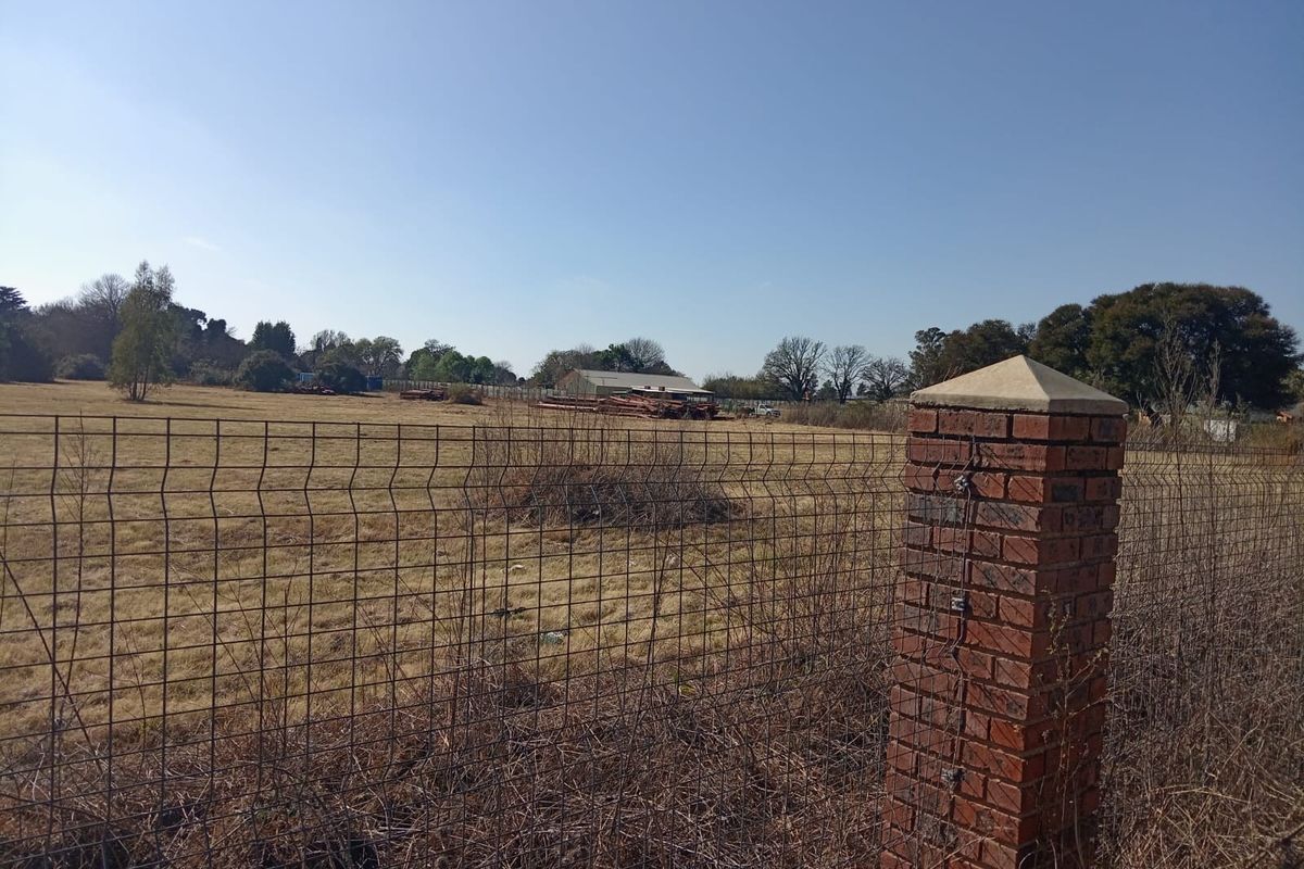 A view of an expansive open plot of land enclosed by wire mesh fencing and a brick pillar.