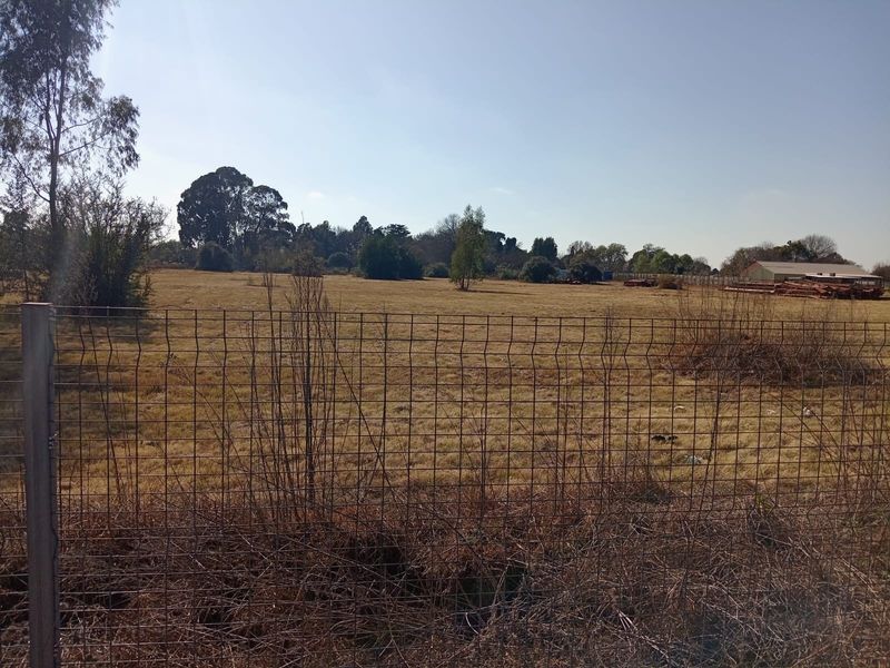 A view of a large, undeveloped plot of land enclosed by wire mesh fencing, featuring dry grass and scattered trees.