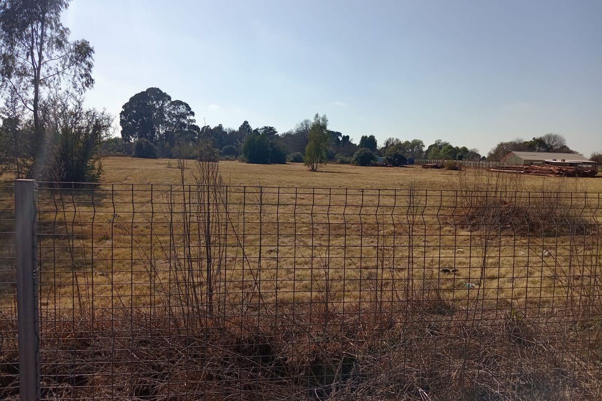 A view of a large, undeveloped plot of land enclosed by wire mesh fencing, featuring dry grass and scattered trees.