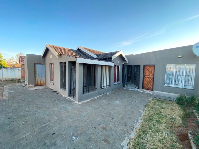 Rear view of the property featuring a paved courtyard, tiled roof, and security fixtures on doors and windows.